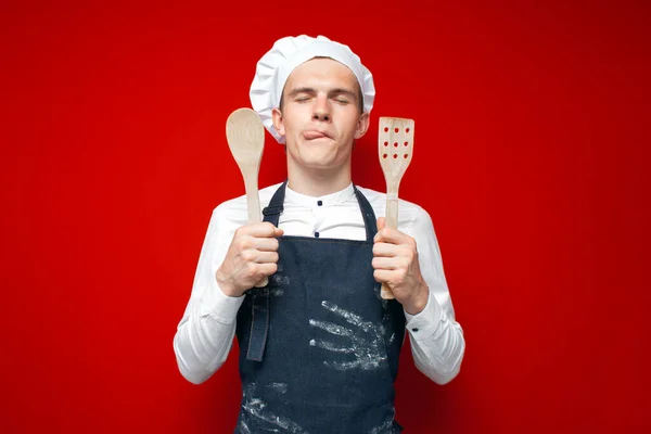 Jovem Cozinheiro Chef Segura Colheres Lamber Lábios Fundo Isolado Vermelho — Fotografia de Stock