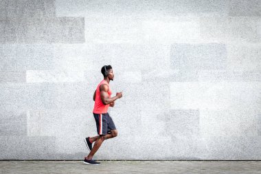 Afro-Amerikalı koşucu şehrin arka planına doğru hızla koşuyor, sporcu treni yolda, genel plan...
