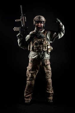 Amerikan askeri üniformalı, tüfekli bir asker gülümsüyor ve siyah bir geçmişe karşı güç gösteriyor. Silahlı bir Amerikan komandosu.