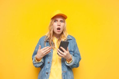 Kot ceketli ve şapkalı genç bir kız elinde akıllı bir telefon tutuyor ve ekranda gösteriyor, şok olmuş hippi kız telefonu kullanıyor.