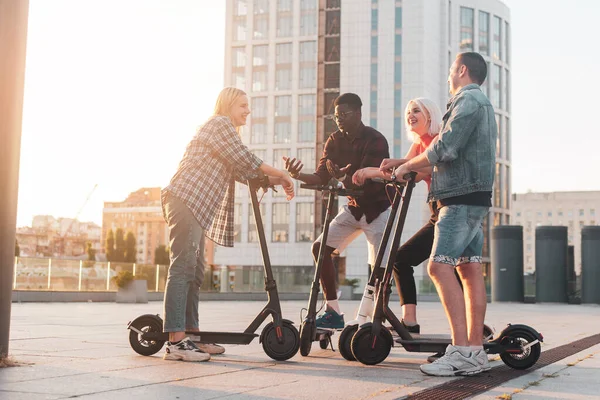 interracial group of young friends ride electric scooters in the city and communicate, multiracial young people use electric vehicles and smiling