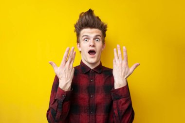 Genç, şaşkın, komik saç stilini sarı izole bir arka planda gösteriyor. Güçlü saç stili olan, şok olmuş bir adam.