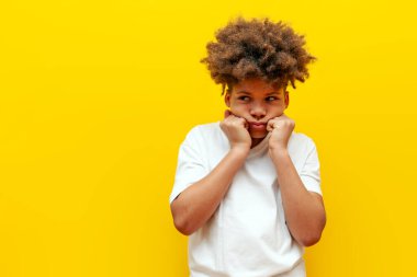 Üzgün kıvırcık Afrikalı Amerikalı çocuk sarı izole edilmiş arka plandan sıkıldı. Beyaz tişörtlü dalgın genç çaresizlik ve yalnızlık içinde fotokopi odasına bakıyor ve düşünüyor.