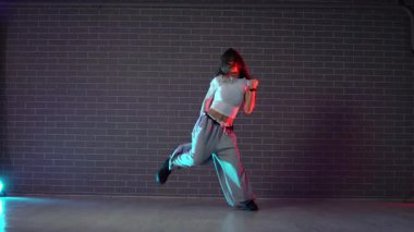 Genç çılgın kız duvarın arkasında dans ediyor. Neon ışıklandırmada arka planda. Kadın koreograf müzik yapıyor ve dans stüdyosunda caz funk 'ı çalıyor.