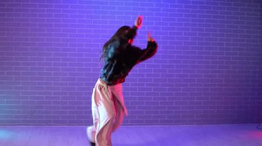 Genç kız koreograf dans ediyor, neon ışıkta hip hop yapıyor, kadın kamera önünde şarkı söylüyor ve karanlık stüdyoda dans çalışıyor.