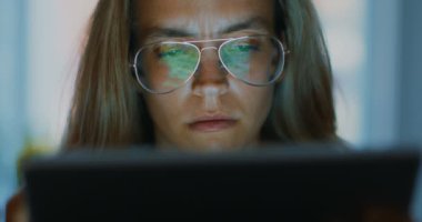 Yüksek kaliteli 4k 12bit görüntüleri. Gözlüklü genç ofis çalışanı dizüstü bilgisayara yazı pişiyor, sorunları çözüyor. Gece yarısı işi. Bilgisayardaki kadın soruna bir çözüm arıyor.