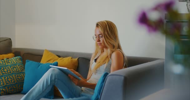 Hochwertige 4k 12bit Filmmaterial von schönen Mädchen mit Tablet-PC sitzt auf der Couch zu Hause. Frau surft im Internet, soziale Netzwerke, sucht etwas im Online-Shop. Filmischer Look — Stockvideo