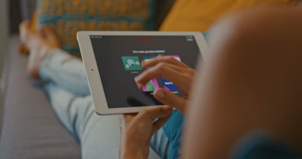 4k 12bit-beeldmateriaal van hoge kwaliteit. Vrouw met behulp van de Netflix-app op witte Tablet-apparaat terwijl zittend op de Bank in de woonkamer. Scrollende Video's, TV-Programma's, afleveringen. Populair op Netflix. Close-up. — Stockvideo