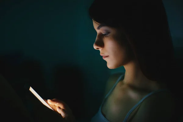 Fiatal gyönyörű nő az ágyban a mobiltelefon késő este a sötét hálószobában, internet függőség koncepció — Stock Fotó