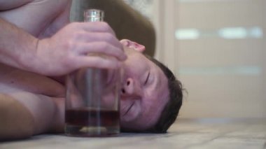 Genç bir sarhoş adam evin yanında bir şişe viski katında uyur.