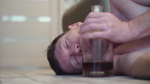 ウイスキーのボトルの横にある家の床の上で眠る若い酔っぱらい — ストック動画