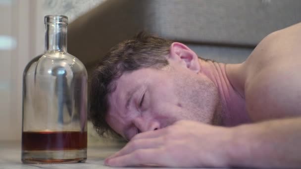 ウイスキーのボトルの横にある家の床の上で眠る若い酔っぱらい — ストック動画