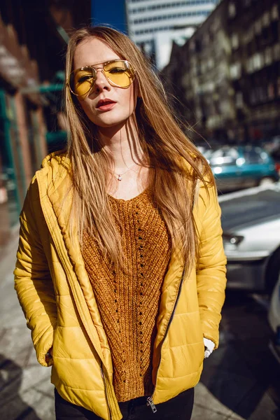 若いヨーロッパ女性は 長いブロンドの髪と 都市センター通り ストリート撮影を歩いて黄色のジャケット 黄色いサングラスを着用します 均一な光 — ストック写真