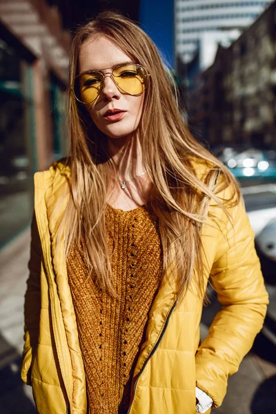 若いヨーロッパ女性は 長いブロンドの髪と 都市センター通り ストリート撮影を歩いて黄色のジャケット 黄色いサングラスを着用します 均一な光 — ストック写真