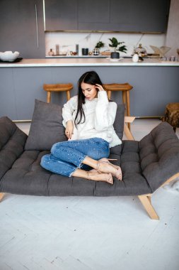 Güzel kız beyaz bir ceket ve kot pantolon kanepeye evde dinleniyor. portre, İskandinav tarzı