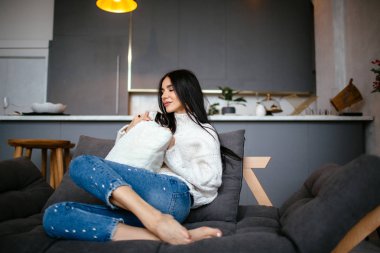 Güzel kız beyaz bir ceket ve kot pantolon kanepeye evde dinleniyor. portre, İskandinav tarzı