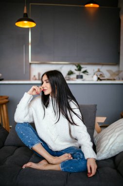 Güzel kız beyaz bir ceket ve kot pantolon kanepeye evde dinleniyor. portre, İskandinav tarzı