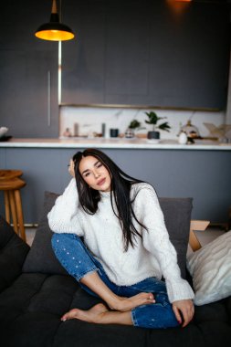 Güzel kız beyaz bir ceket ve kot pantolon kanepeye evde dinleniyor. portre, İskandinav tarzı