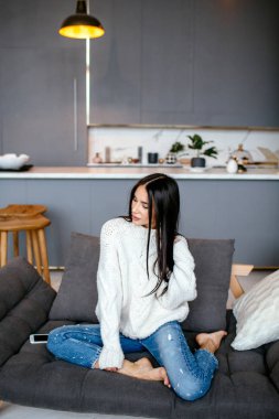 Güzel kız beyaz bir ceket ve kot pantolon kanepeye evde dinleniyor. portre, İskandinav tarzı