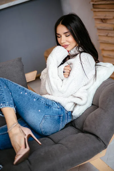 穿着白色夹克和牛仔裤的美丽女孩正在家里的沙发上休息 肖像画 斯堪的纳维亚风格 — 图库照片
