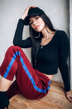 Bir kap ve spor giyim esmer kız portresi. Doğal ışık. Kırmızı eşofman altı, siyah en iyi, siyah başlığı.