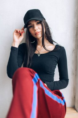 Bir kap ve spor giyim esmer kız portresi. Doğal ışık. Kırmızı eşofman altı, siyah en iyi, siyah başlığı.