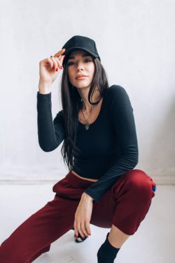 Bir kap ve spor giyim esmer kız portresi. Doğal ışık. Kırmızı eşofman altı, siyah en iyi, siyah başlığı.