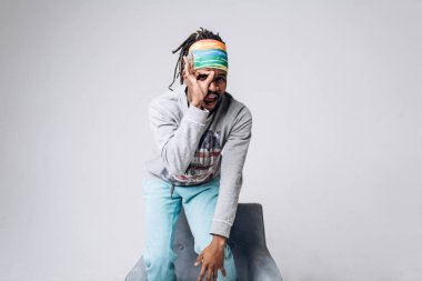 Bir gri kazak ve mavi pantolon sandalye yakınındaki gri bir arka plan üzerine siyah bir gülümseyen portre genç model