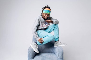 Bir gri kazak ve mavi pantolon sandalye yakınındaki gri bir arka plan üzerine siyah bir gülümseyen portre genç model