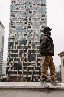 Yakışıklı Afrika kökenli Amerikalı dreadlocks kahverengi pantolon ve başını evleri, arka planı siyah şapkalı Mavi kazak ile şehir