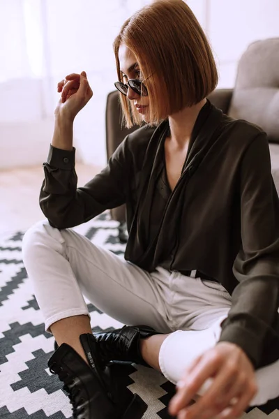 Belle fille douce couchée sur le canapé. Modèle élégant doré avec cheveux courts roux, lèvres dodues, lunettes de soleil, vêtements décontractés, costume, tenue, salopettes. Test de modèle, lunettes publicitaires, vêtements — Photo