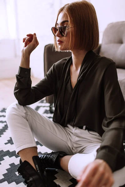 Belle fille douce couchée sur le canapé. Modèle élégant doré avec cheveux courts roux, lèvres dodues, lunettes de soleil, vêtements décontractés, costume, tenue, salopettes. Test de modèle, lunettes publicitaires, vêtements — Photo