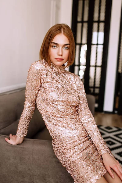 Güzel tatlı kız profesyonel kamera poz. Kısa kırmızı saçlı altın şık model, tam dudaklar, güzel bir altın zarif gece elbisesi, gece elbisesi giymiş. Model testi, giyim adve