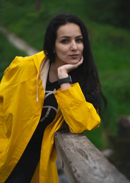 beautiful young girl in a yellow raincoat, with an umbrella in the garden, rainy spring, beautiful and stylish clothes, fashion