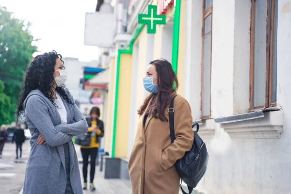 beautiful ladies talking near the pharmacy on the street, wearing medicine masks due to coronavirus, protection from the virus, keeping the distance