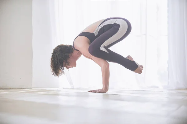 Bela jovem pratica ioga asana bakasana - pose de guindaste no estúdio de ioga luz — Fotografia de Stock