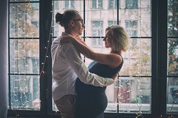 Homem e mulher grávida dançam perto da janela na sala de estilo loft — Fotografia de Stock