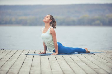 Güzel ve genç birbayan uygulamaları yoga asana köpek göl yakınındaki ahşap güverte üzerinde yukarı bakacak şekilde