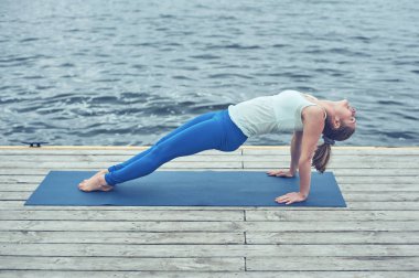 Güzel ve genç birbayan uygulamaları yoga asana Purvottanasana yukarı doğru tahta poz göl yakınındaki ahşap güverte