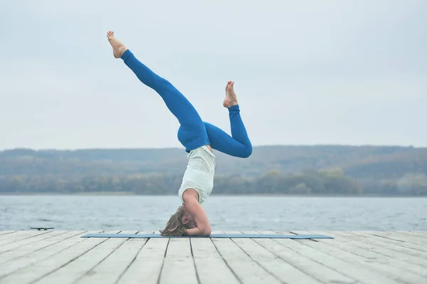 Krásná mladá žena praktiky jóga asana Shirshasana - stoj pozice na dřevěnou terasu u jezera — Stock fotografie