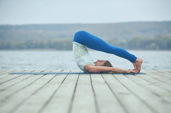 Красивая молодая женщина практикует йогу asana Shirshasana - Поза стойки на деревянной палубе возле озера — стоковое фото