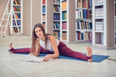 Güzel genç kadın kitap ve uygulamaları yoga asana Samakonasana düz açı duruş kütüphanede okuma