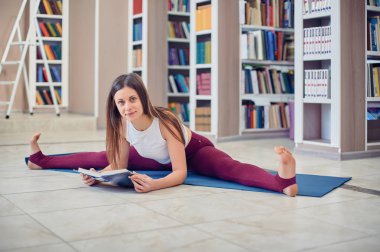 Güzel genç kadın kitap ve uygulamaları yoga asana Samakonasana düz açı duruş kütüphanede okuma