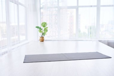 Modern dairede büyük ışıklı pencereli yoga odası. Beyaz zeminde yoga minderi var, insan yok.