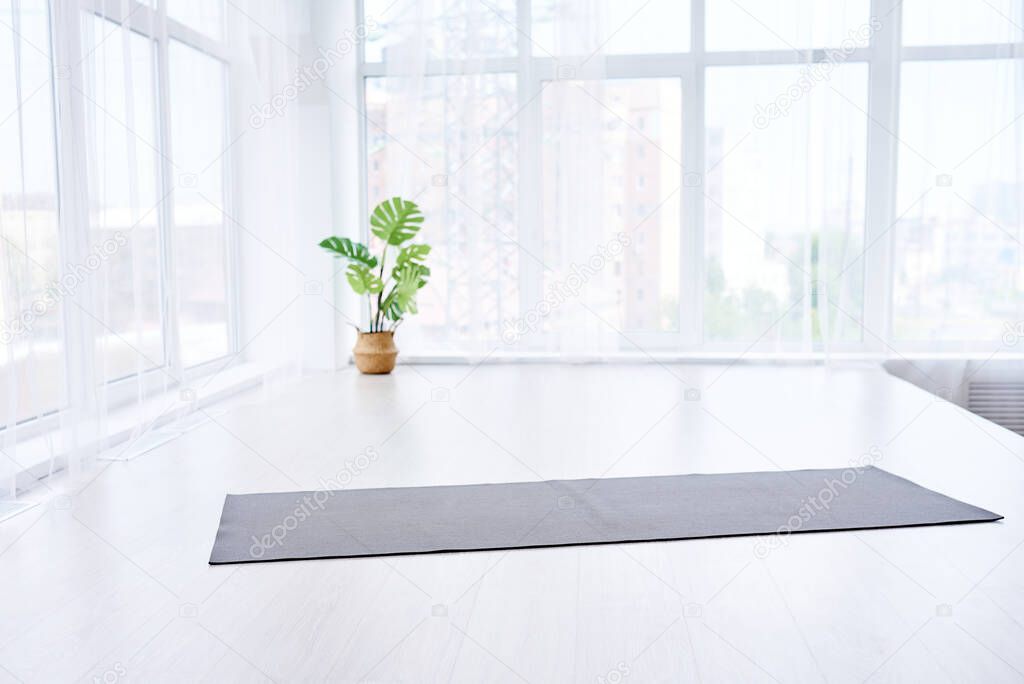 yoga room with big light window in modern flat. Yoga mat on the white floor, no people