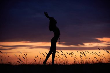 Genç ve güzel bir kadının silueti geceleri dışarıda yoga yapıyor.