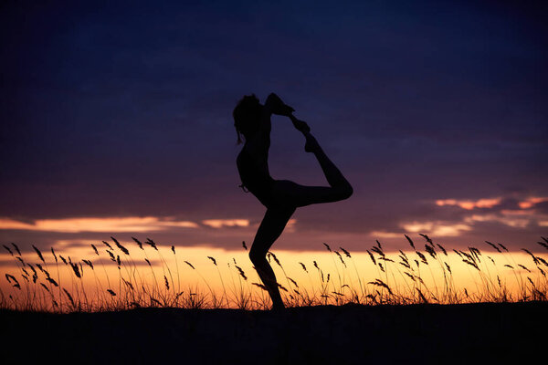 Silhouette of a beautiful young woman practices yoga outdoor at night