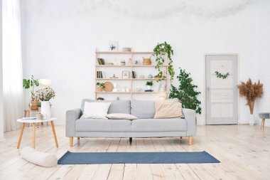 Modern beyaz dairede büyük ışıklı pencereli yoga odası. Yerde yoga minderi var, insan yok.