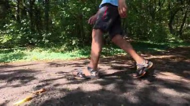 Çocuğun ormanda şort ve sandalet giyerek yürüdüğü yakın plan. Açık hava macerası, doğa yürüyüşü ve keşfi..