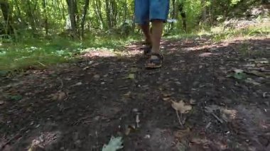 Çocuğun ormanda şort ve sandalet giyerek yürüdüğü yakın plan. Açık hava macerası, doğa yürüyüşü ve keşfi..